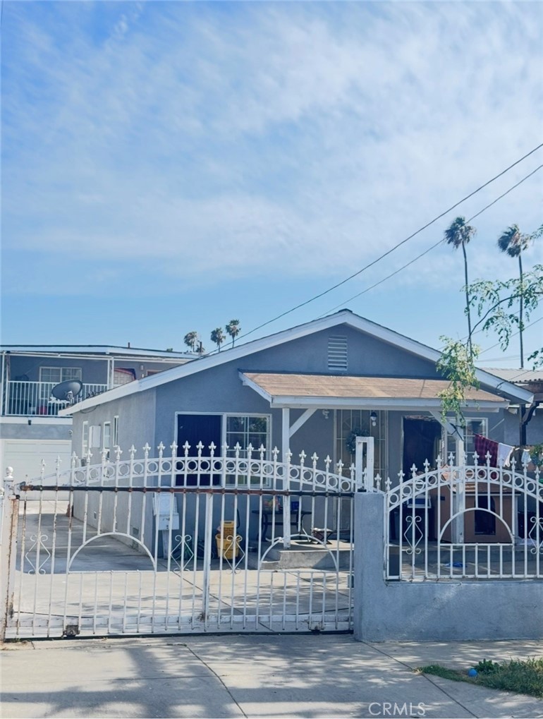 Street-front view of 4132 W 105th St, the single-story blue-gray front unit behind a white wrought-iron gate and fence, with palm trees behind