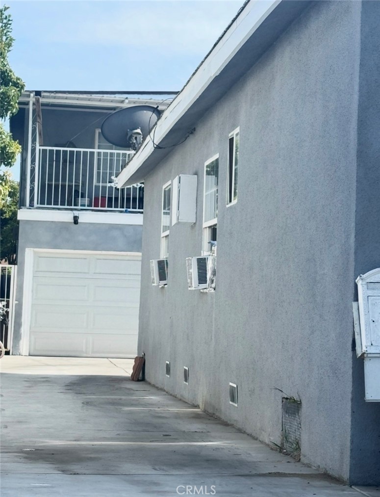 Side elevation of the two-story rear unit, showing the stucco flank wall, upstairs balcony with railing, window units, and the garage and gate beyond