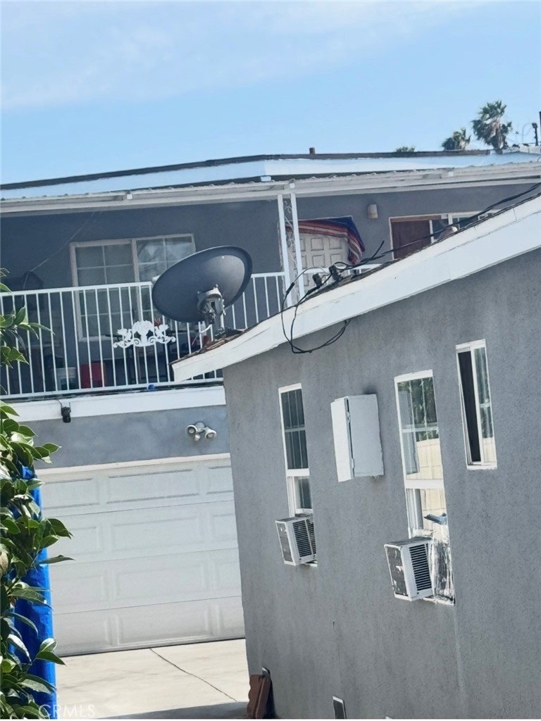 Close upward view of the rear unit's upstairs balcony with its metal railing and satellite dish, the two-car garage door below, and window air-conditioning units