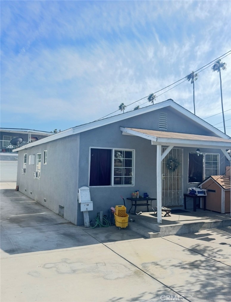 Front three-quarter elevation of 4132 W 105th St, a single-story blue-gray stucco bungalow with a gabled covered porch and palm trees against a blue sky in Lennox, Inglewood